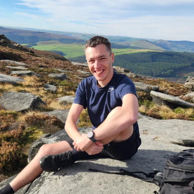 Chris Davidson sitting on the gritstone of Derwent Edge, with the valley behind
